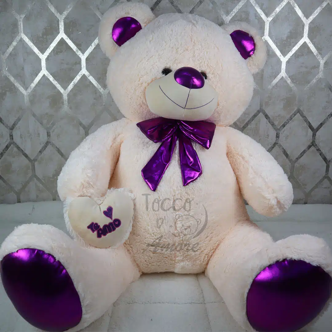 Precio de un oso gigante en Colombia: oso de peluche crema de 1,85 m con moño morado metalizado y corazón bordado con «Te amo»