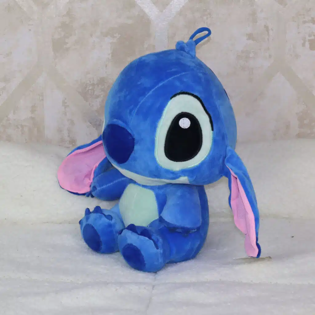 Peluche azul de 30 cm inspirado en Stitch, sentado sobre una cama