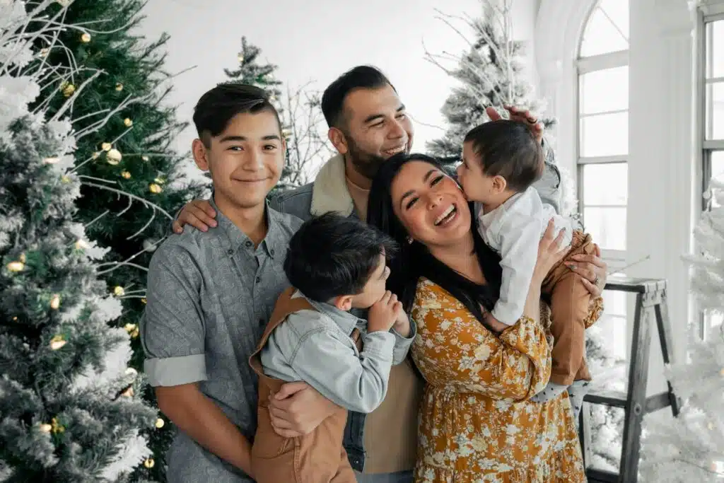 Familia latina abrazada y riendo junto al árbol de Navidad