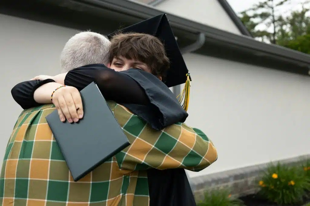 Graduado con toga, birrete y diploma abraza a un familiar a la salida de la ceremonia