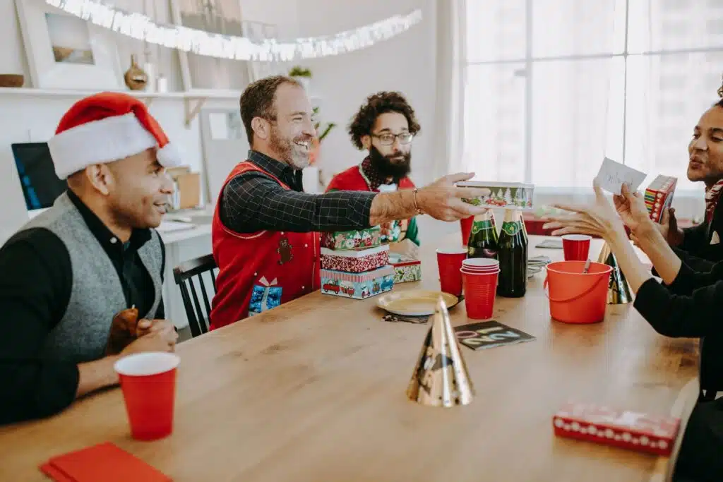 Grupo de compañeros intercambia regalos de amigo secreto alrededor de una mesa en la fiesta de fin de año