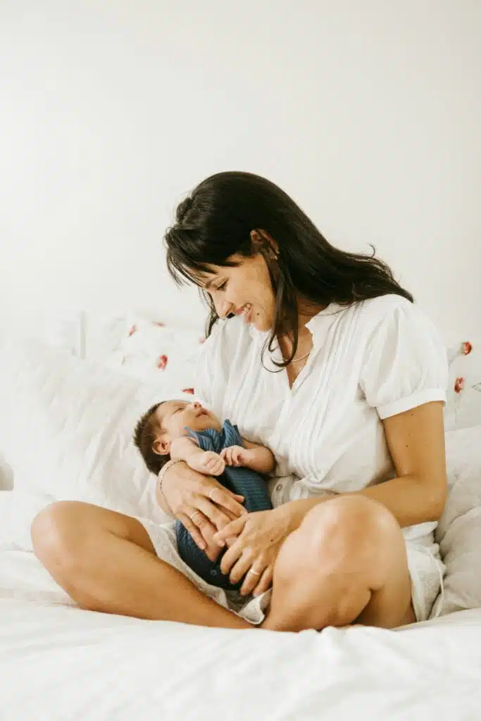 Mamá primeriza sentada en la cama mira a su bebé recién nacido en brazos