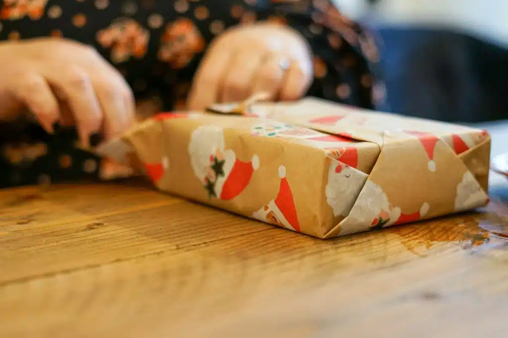 Manos envolviendo un regalo de Navidad en papel kraft sobre una mesa de madera