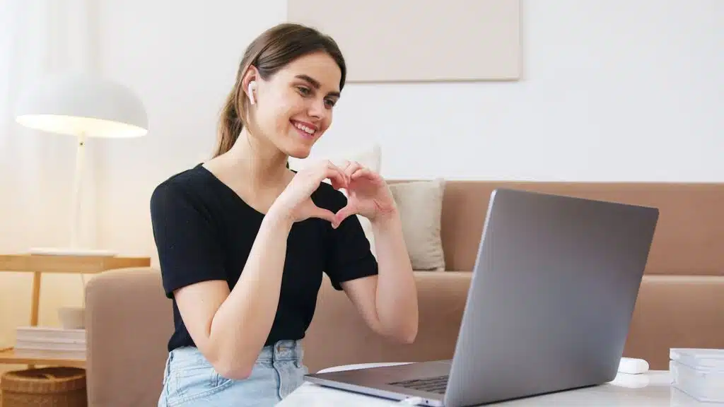 Mujer hace un corazón con las manos durante una videollamada con su pareja a distancia