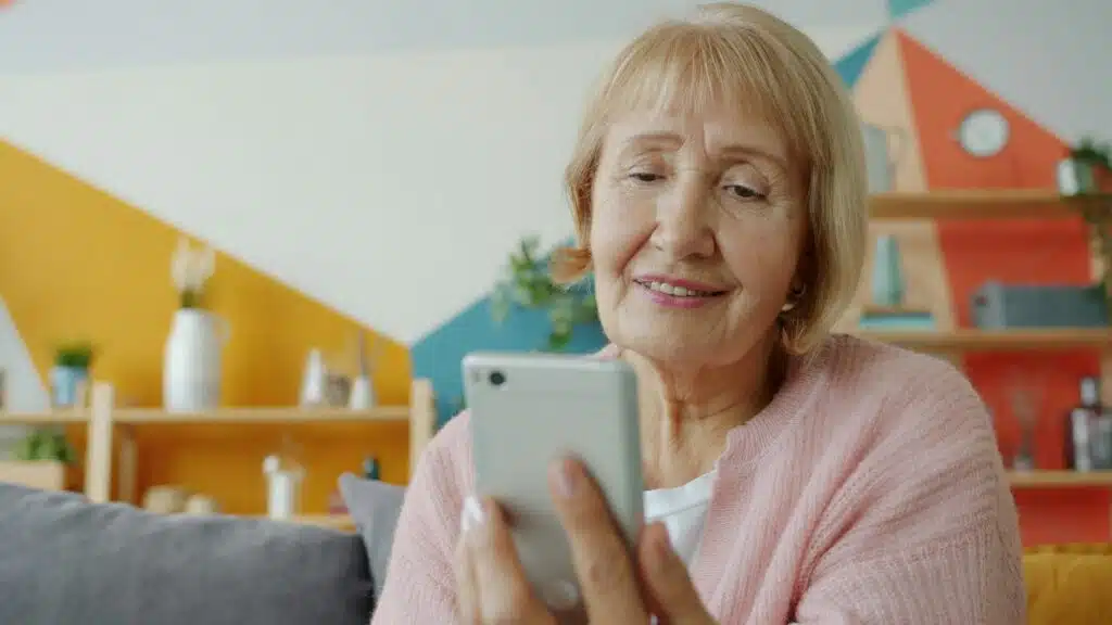 Mujer mayor sonríe mientras escucha un audio en su celular, una voz querida guardada en el teléfono