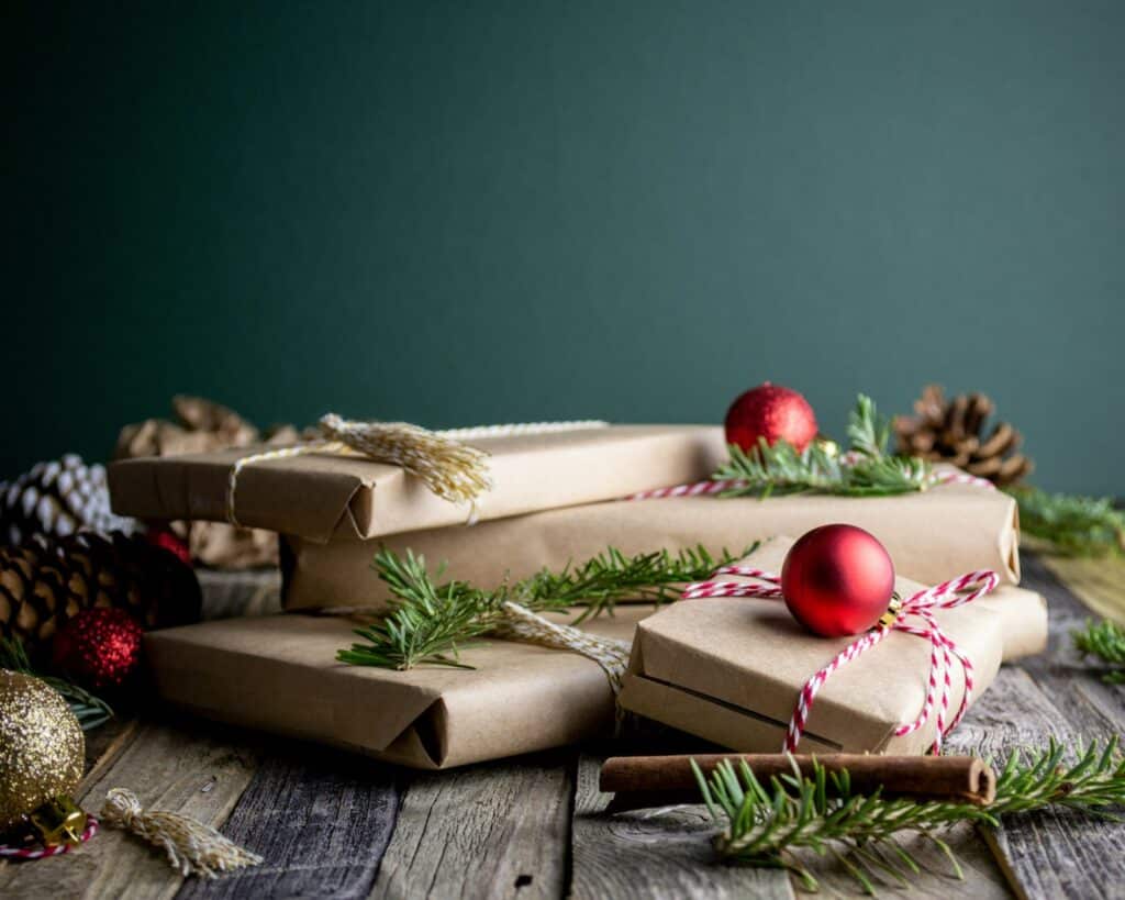 Regalos de Navidad envueltos en papel kraft con ramas de pino y bolas rojas sobre una mesa de madera