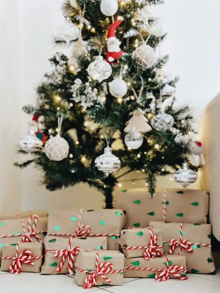Varios regalos de Navidad envueltos en papel kraft con cinta roja y blanca bajo el árbol